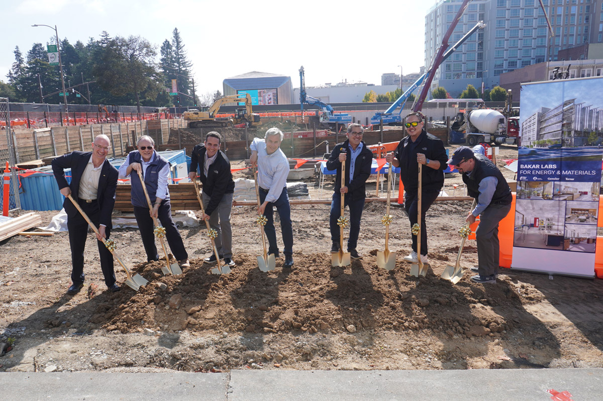 Seven men standing in dirt field holding shovels spray-painted gold