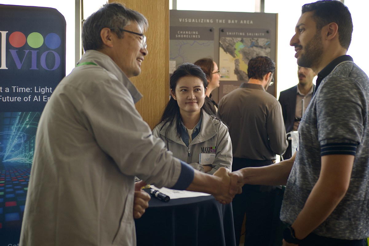 Two men shaking hands with other people in the background at a conference