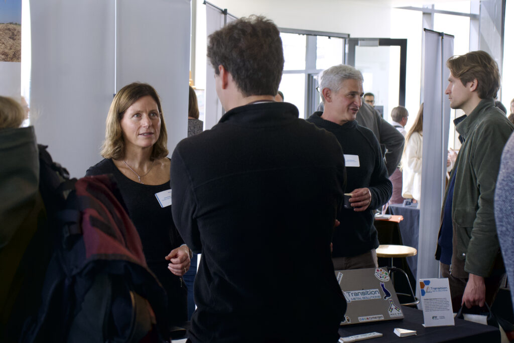 Transition Metal Solutions CCO Vania Grandi, left, and CEO Sasha Milshteyn, right, stand talking to two attendees.