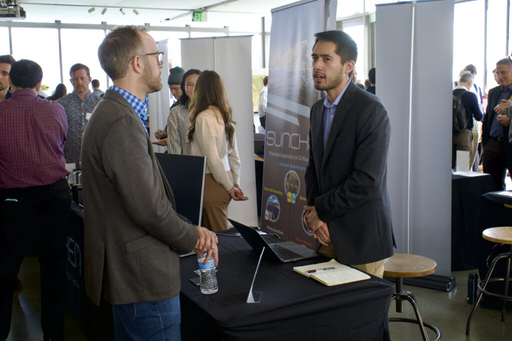 WattUp Energy CEO Aaron Garg stands behind a table, talking to an attendee.